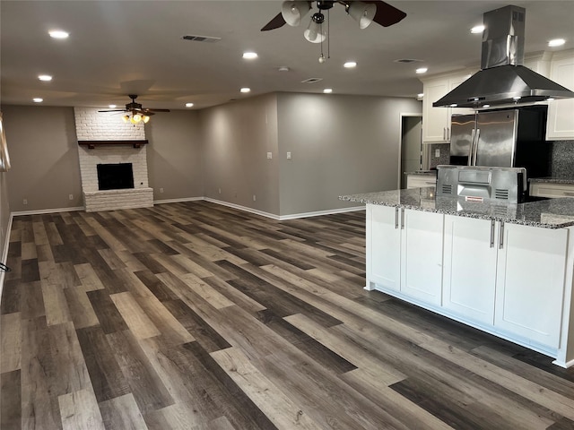 kitchen featuring light stone countertops, a brick fireplace, island exhaust hood, decorative backsplash, and white cabinets