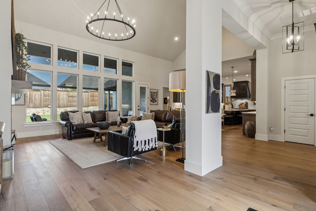 living area featuring a chandelier, baseboards, light wood-style flooring, and a high ceiling