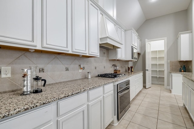 kitchen with stainless steel appliances, white cabinets, light stone counters, vaulted ceiling, and light tile patterned flooring