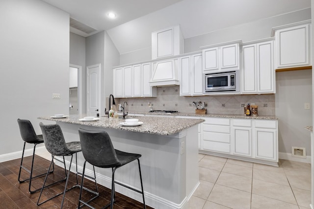 kitchen featuring appliances with stainless steel finishes, an island with sink, decorative backsplash, white cabinets, and custom exhaust hood