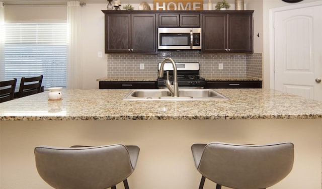 kitchen featuring decorative backsplash, dark brown cabinets, stainless steel appliances, and a kitchen bar