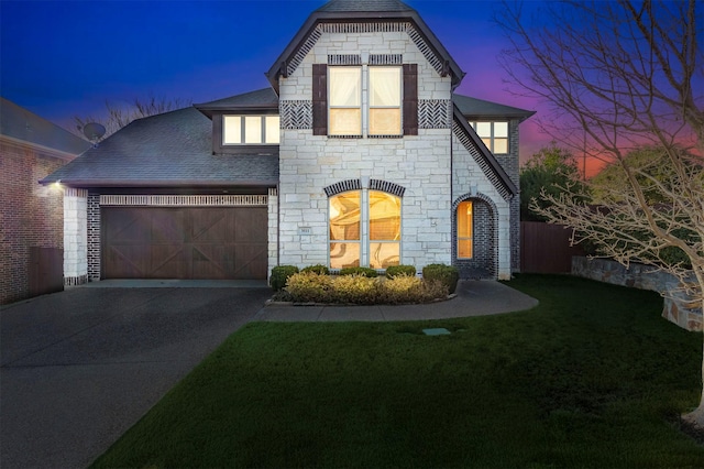 view of front of home with a garage, driveway, stone siding, roof with shingles, and a front lawn