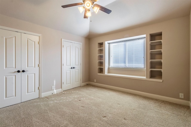 unfurnished bedroom featuring carpet floors, two closets, vaulted ceiling, ceiling fan, and baseboards