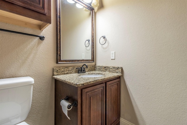 half bath with toilet, a textured wall, and vanity