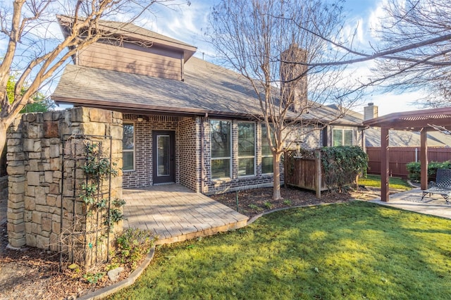 back of house featuring roof with shingles, brick siding, a lawn, fence, and a pergola