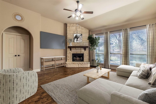 living room featuring vaulted ceiling, ceiling fan, dark hardwood / wood-style floors, and a stone fireplace