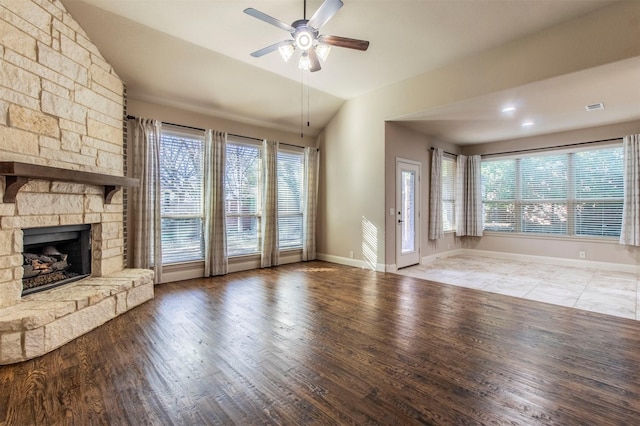 unfurnished living room with ceiling fan, vaulted ceiling, a stone fireplace, and hardwood / wood-style floors