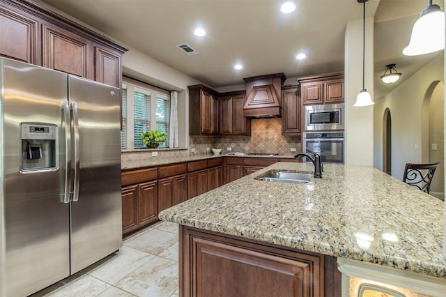 kitchen with decorative backsplash, custom range hood, light stone counters, appliances with stainless steel finishes, and a sink