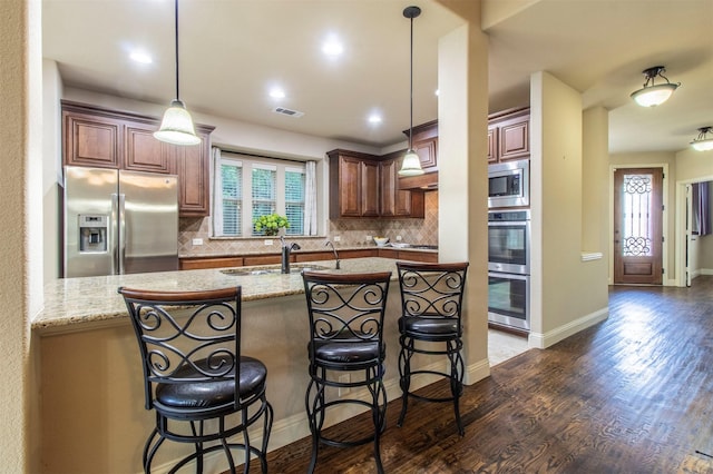 kitchen featuring stainless steel appliances, tasteful backsplash, dark wood-type flooring, a sink, and a kitchen breakfast bar