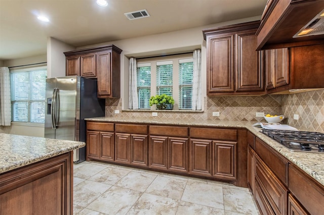 kitchen featuring visible vents, appliances with stainless steel finishes, backsplash, light stone countertops, and custom range hood