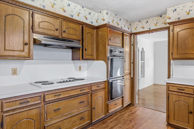 kitchen with white electric cooktop, light hardwood / wood-style flooring, black double oven, and a textured ceiling