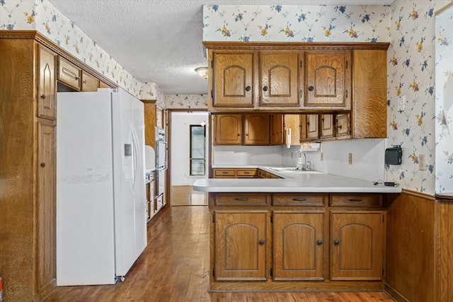 kitchen featuring sink, white fridge with ice dispenser, stainless steel double oven, a textured ceiling, and light hardwood / wood-style flooring