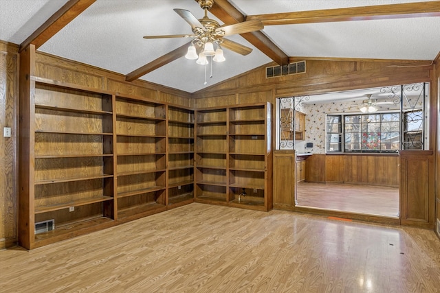 interior space featuring vaulted ceiling with beams, a textured ceiling, wooden walls, and light hardwood / wood-style flooring