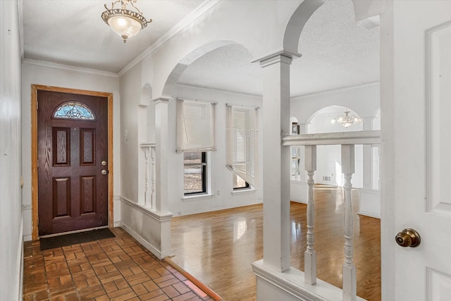 entryway featuring ornamental molding, a textured ceiling, and ornate columns