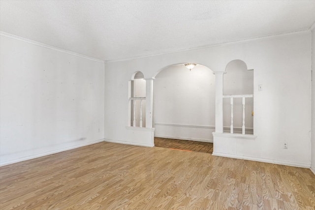 empty room featuring ornamental molding, ornate columns, a textured ceiling, and light wood-type flooring