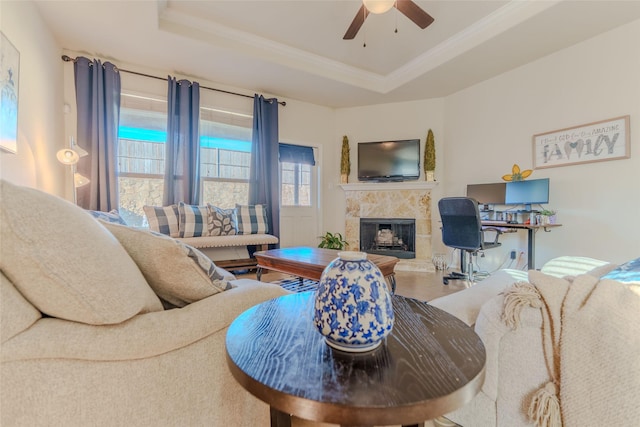 living area with a raised ceiling, ornamental molding, a high end fireplace, light tile patterned flooring, and ceiling fan