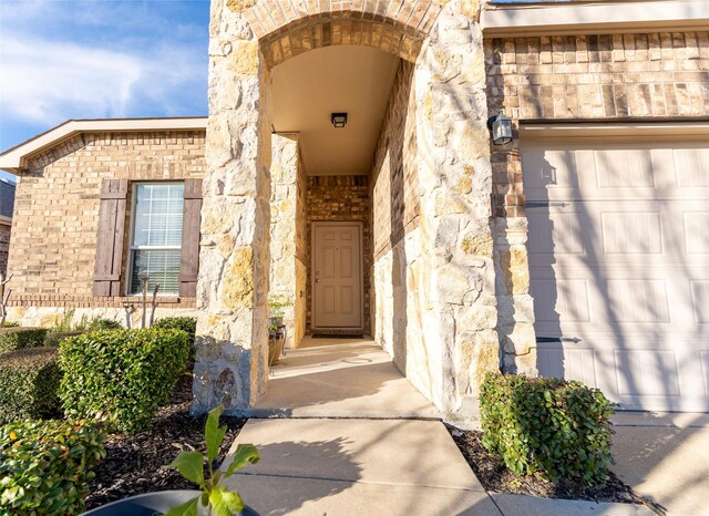 entrance to property with a garage, stone siding, and brick siding