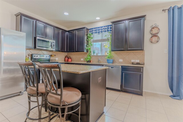 kitchen featuring tasteful backsplash, a kitchen island, stainless steel appliances, a kitchen bar, and light tile patterned flooring