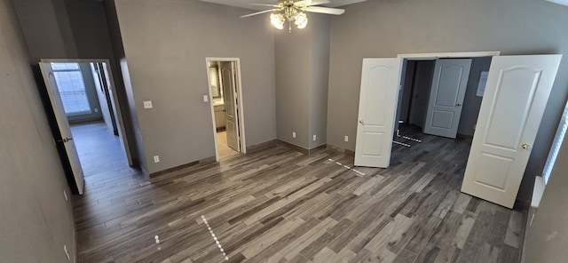 unfurnished bedroom with connected bathroom, ceiling fan, dark wood-type flooring, and a high ceiling