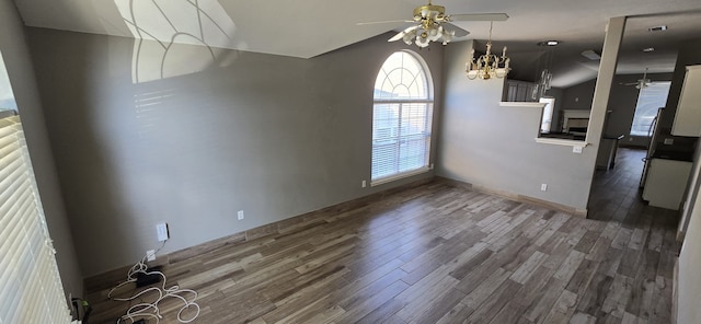 unfurnished dining area with hardwood / wood-style floors, ceiling fan with notable chandelier, and vaulted ceiling