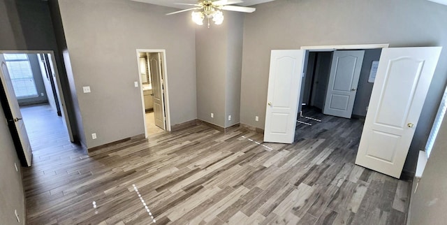 unfurnished bedroom with ceiling fan, a towering ceiling, wood-type flooring, and connected bathroom