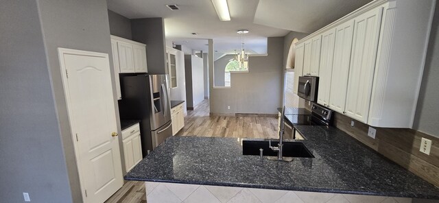 kitchen featuring stainless steel fridge, black range with electric stovetop, sink, dark stone countertops, and white cabinetry