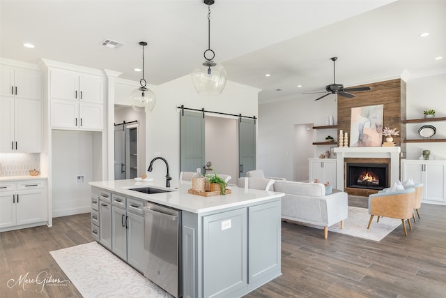 kitchen with stainless steel dishwasher, sink, a barn door, a center island with sink, and hanging light fixtures