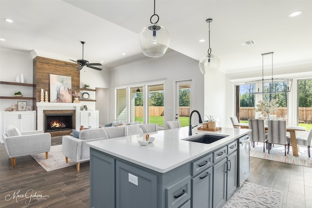 kitchen with pendant lighting, dishwasher, sink, ornamental molding, and a center island with sink