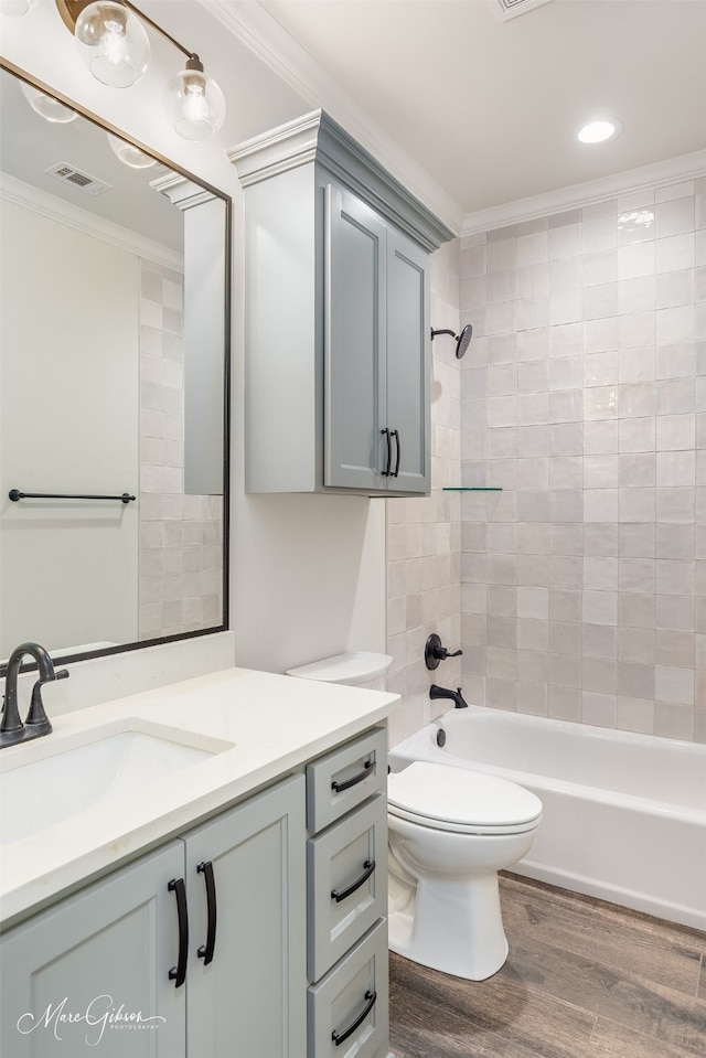 full bathroom featuring crown molding, hardwood / wood-style floors, vanity, tiled shower / bath, and toilet