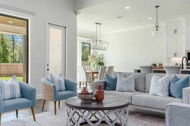 tiled living room featuring a notable chandelier, ornamental molding, sink, and a healthy amount of sunlight