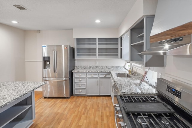 kitchen featuring exhaust hood, light stone countertops, sink, and appliances with stainless steel finishes