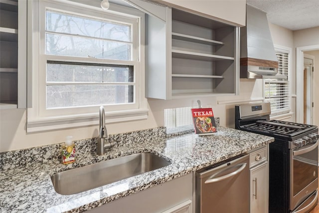 kitchen featuring light stone counters, sink, wall chimney range hood, and stainless steel appliances