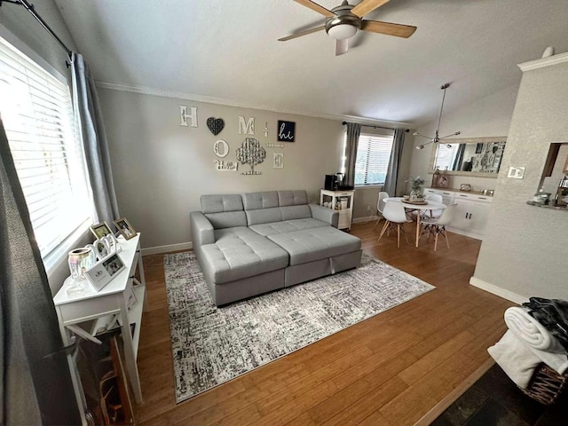 living room featuring ceiling fan, dark hardwood / wood-style flooring, ornamental molding, and vaulted ceiling