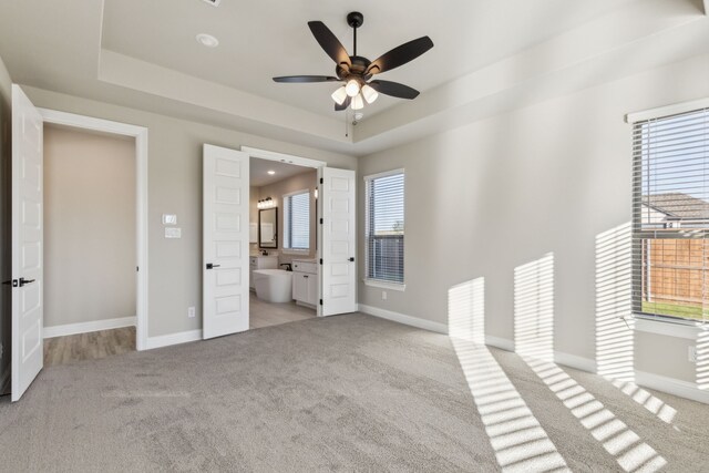 unfurnished bedroom with ceiling fan, ensuite bathroom, light carpet, and a tray ceiling