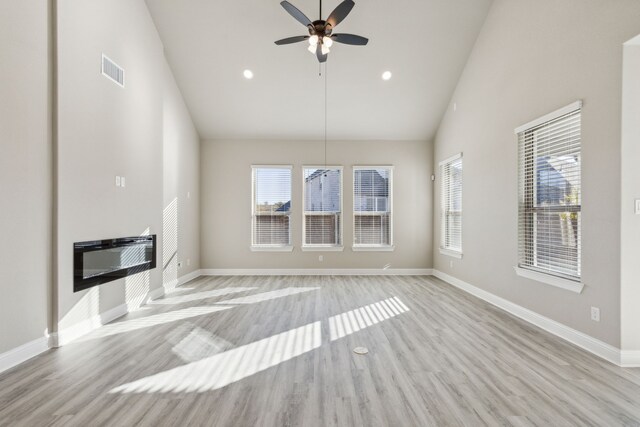 unfurnished living room featuring plenty of natural light, ceiling fan, light wood-type flooring, and lofted ceiling