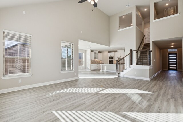 unfurnished living room featuring ceiling fan, light hardwood / wood-style floors, and a towering ceiling