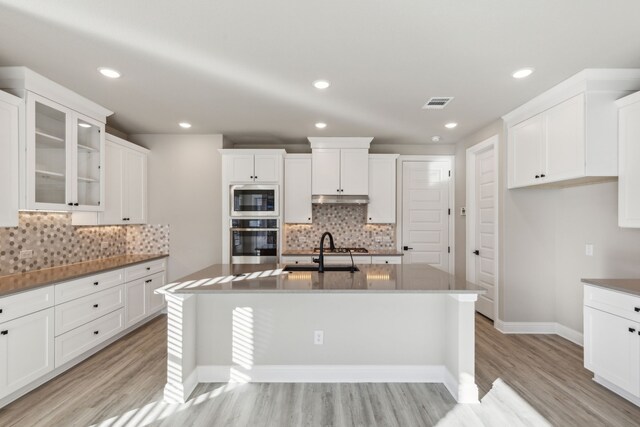 kitchen featuring sink, light wood-type flooring, stainless steel appliances, and an island with sink