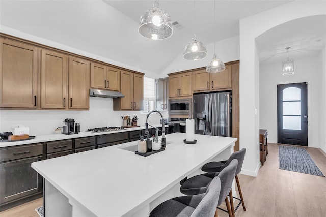 kitchen with sink, stainless steel appliances, pendant lighting, a kitchen island with sink, and a breakfast bar