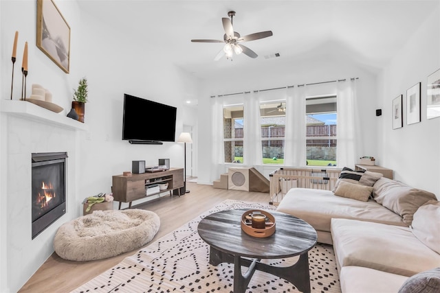 living room with ceiling fan, a tiled fireplace, and light hardwood / wood-style flooring