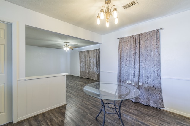 unfurnished dining area featuring ceiling fan with notable chandelier, dark hardwood / wood-style flooring, and a textured ceiling