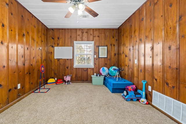 rec room with ceiling fan, carpet floors, and wooden walls