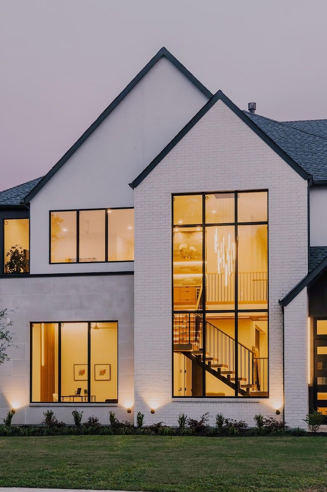 back house at dusk featuring a lawn