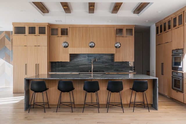 kitchen with a kitchen bar, a large island with sink, beam ceiling, and dark stone countertops