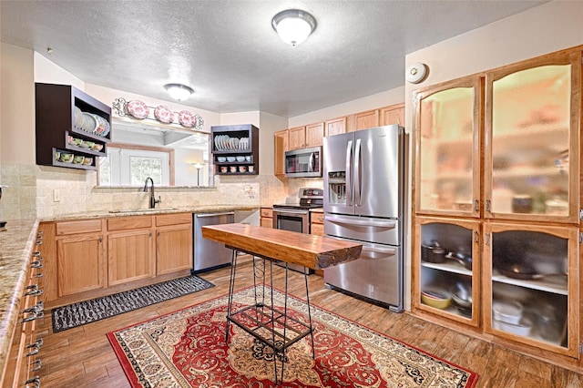 kitchen with light wood finished floors, a sink, a textured ceiling, appliances with stainless steel finishes, and tasteful backsplash