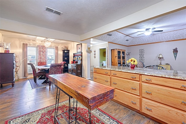 kitchen featuring a textured ceiling, ornamental molding, dark wood-type flooring, visible vents, and a ceiling fan