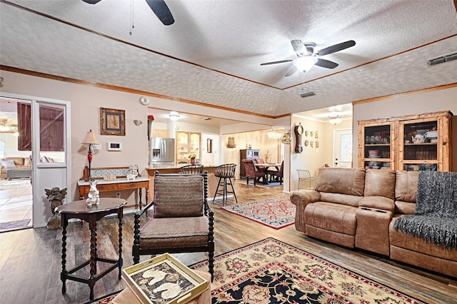 living area featuring ceiling fan, a textured ceiling, wood-type flooring, and visible vents