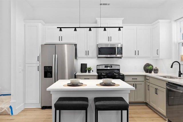 kitchen with sink, light hardwood / wood-style flooring, appliances with stainless steel finishes, decorative light fixtures, and white cabinetry