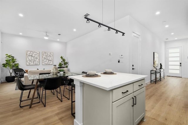 kitchen with ceiling fan, a center island, light hardwood / wood-style flooring, gray cabinets, and a breakfast bar