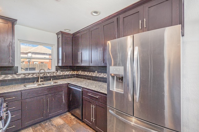 kitchen featuring backsplash, sink, light stone countertops, dark brown cabinetry, and stainless steel appliances