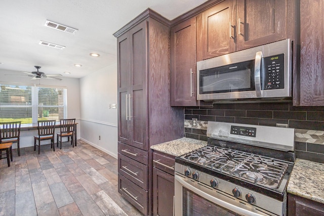 kitchen featuring backsplash, light stone counters, dark brown cabinets, stainless steel appliances, and hardwood / wood-style floors